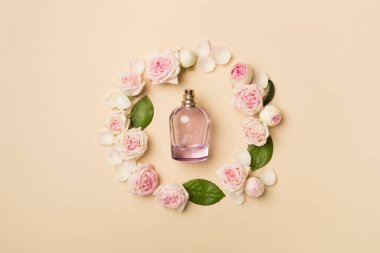 Bottle of perfume with rose flowers on color background, top view.