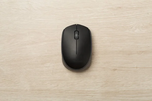 Black wireless mouse on wooden background, top view.