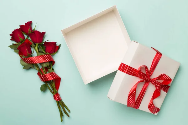 Open gift box with red roses on color background, top view