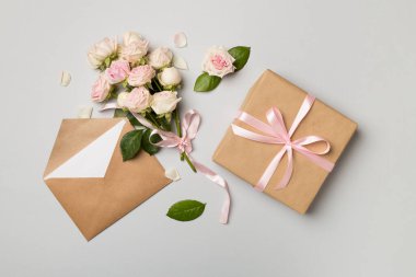 Envelope, gift box and rose flowers on color background, top view.