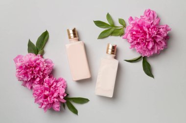 Renkli arka planda kozmetik şişeleri ve şakayık çiçekleri olan düz kompozisyon, üst görünüm.