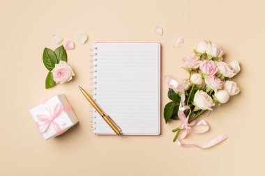 Notebook, gift box and rose flowers on color background, top view.