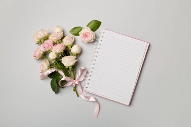 Notebook, gift box and rose flowers on color background, top view.