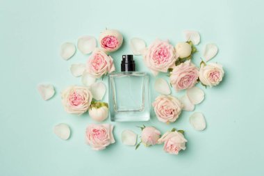 Bottle of perfume with rose flowers on color background, top view.