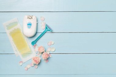 Wax strips, modern epilator and razor with flowers on wooden background, top view.