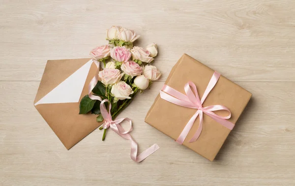 Envelope, gift box and rose flowers on wooden background, top view.