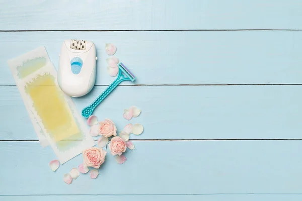 stock image Wax strips, modern epilator and razor with flowers on wooden background, top view.