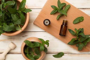 Melissa essential oil bottles with mortar pestle on wooden background, top view.