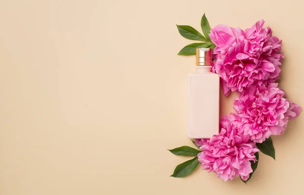Cosmetic bottle with peony flower on color background, top view.