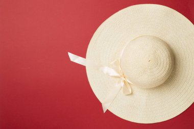 Beautiful straw hat with ribbon and bow on color background, top view.