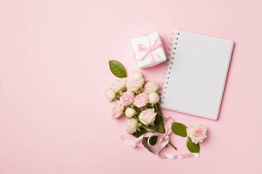 Notebook, gift box and rose flowers on color background, top view.