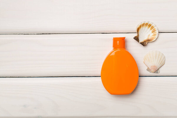 Бутылка с солнцезащитным кремом и раковинами на деревянном фоне, вид сверху.