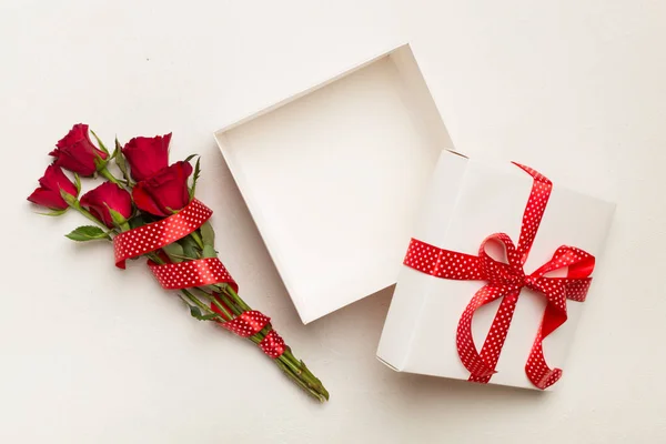 Open gift box with red roses on wooden background, top view
