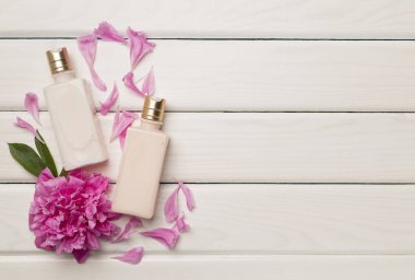 Ahşap arka planda kozmetik şişeleri ve şakayık çiçekleri olan düz kompozisyon, üst görünüm.