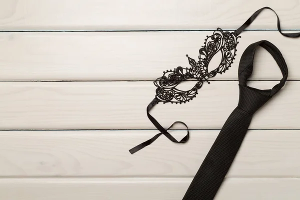 stock image Lace mask and tie on wooden background, top view.