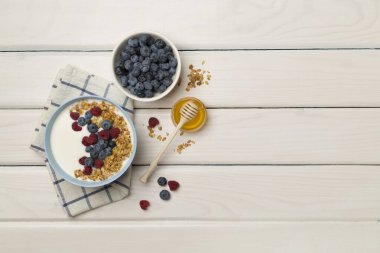 Bowl with granola, yogurt and fresh berries on wooden background, top view.