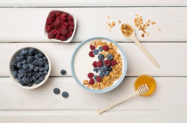 Bowl with granola, yogurt and fresh berries on wooden background, top view.