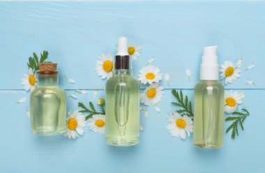 Papatya çayı şişeleri ve ahşap arka planda çiçekler, üst manzara.