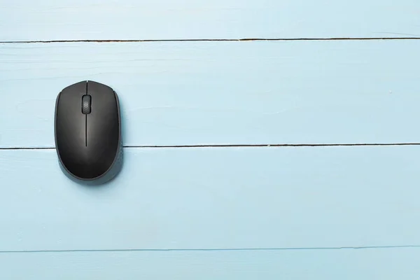 Black wireless mouse on wooden background, top view.