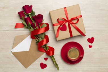 Ahşap zemin üzerinde güller olan kırmızı kahve fincanı, üst manzara.