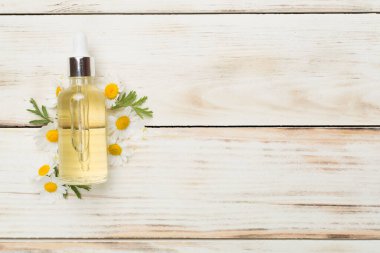 Şişe papatya çayı esaslı yağ ve ahşap arka planda çiçekler, üst manzara.