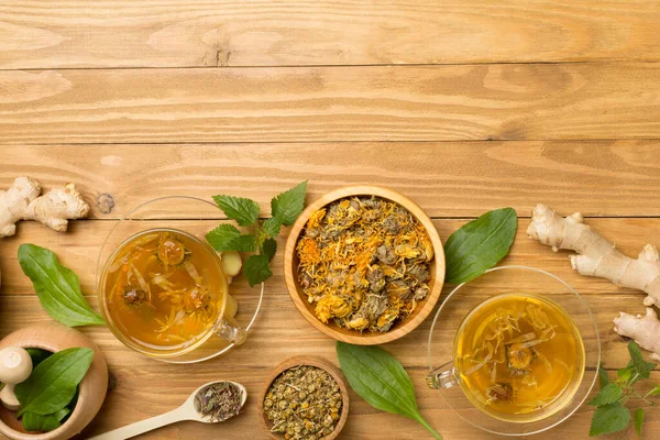 Herbal tea with ingredients on wooden background, top view.