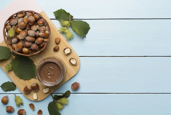 stock image Hazelnut cream with nuts and green leaves on wooden background, top view.