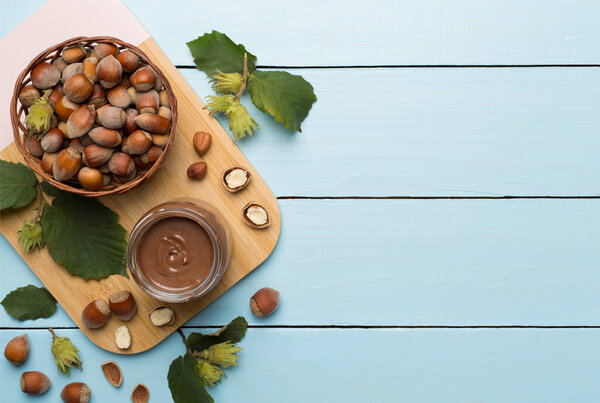 Hazelnut cream with nuts and green leaves on wooden background, top view.