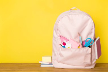 Ahşap masada kırtasiye malzemesi olan pembe okul çantası.