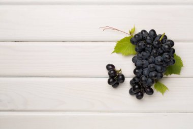 Ahşap zemin üzerinde yaprakları olan bir demet olgun koyu mavi üzüm..