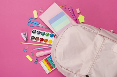 Renkli arka planda kırtasiye malzemesi olan pembe okul çantası, üst görünüm