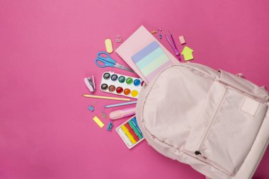 Renkli arka planda kırtasiye malzemesi olan pembe okul çantası, üst görünüm