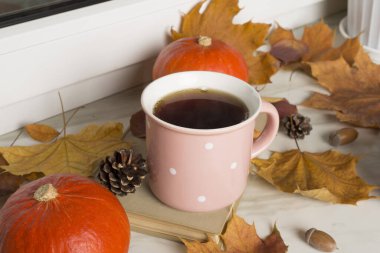 Pencere kenarında balkabaklı ve sonbahar yapraklı bir fincan çay..