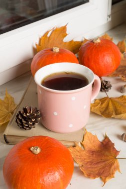 Pencere kenarında balkabaklı ve sonbahar yapraklı bir fincan çay..