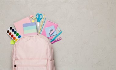 Beton zemin üzerinde kırtasiye malzemesi olan pembe okul çantası, üst görünüm