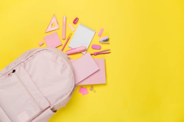 Renkli arka planda kırtasiye malzemesi olan pembe okul çantası, üst görünüm