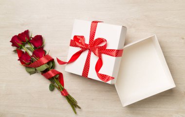 Open gift box with red roses on wooden background, top view
