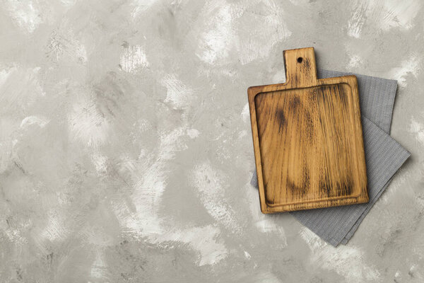 Cutting board with towel on concrete background, top view.