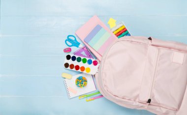 Ahşap zemin üzerinde kırtasiye malzemesi olan pembe okul çantası.