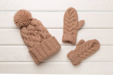 Brown winter hat and mittens on wooden background. Top view