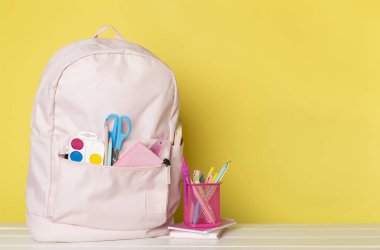 Ahşap masada kırtasiye malzemesi olan pembe okul çantası.