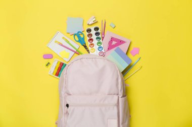 Renkli arka planda kırtasiye malzemesi olan pembe okul çantası, üst görünüm