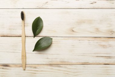 Toothbrush with green leaves wooden on background. Top view