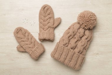 Brown winter hat and mittens on wooden background. Top view