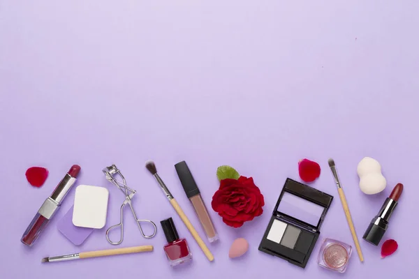Flat lay with makeup products and tools with flowers on color background