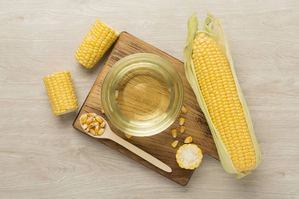 Corn oil with fresh cobs on wooden background, top view