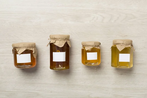 Jars with different honey on wooden background, top view. Mock up design