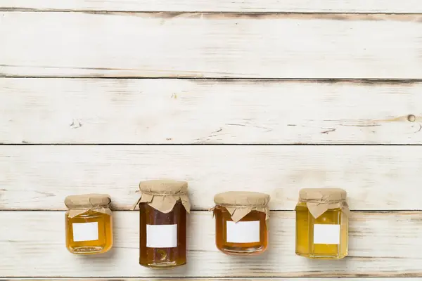 Jars with different honey on wooden background, top view. Mock up design