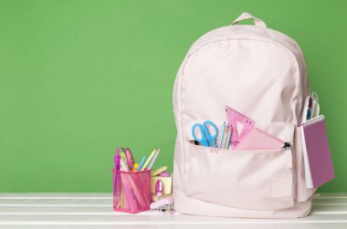 Ahşap masada kırtasiye malzemesi olan pembe okul çantası.