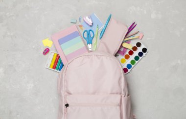 Pembe okul sırt çantası, arka planda kırtasiye malzemesi, üst görünüm.